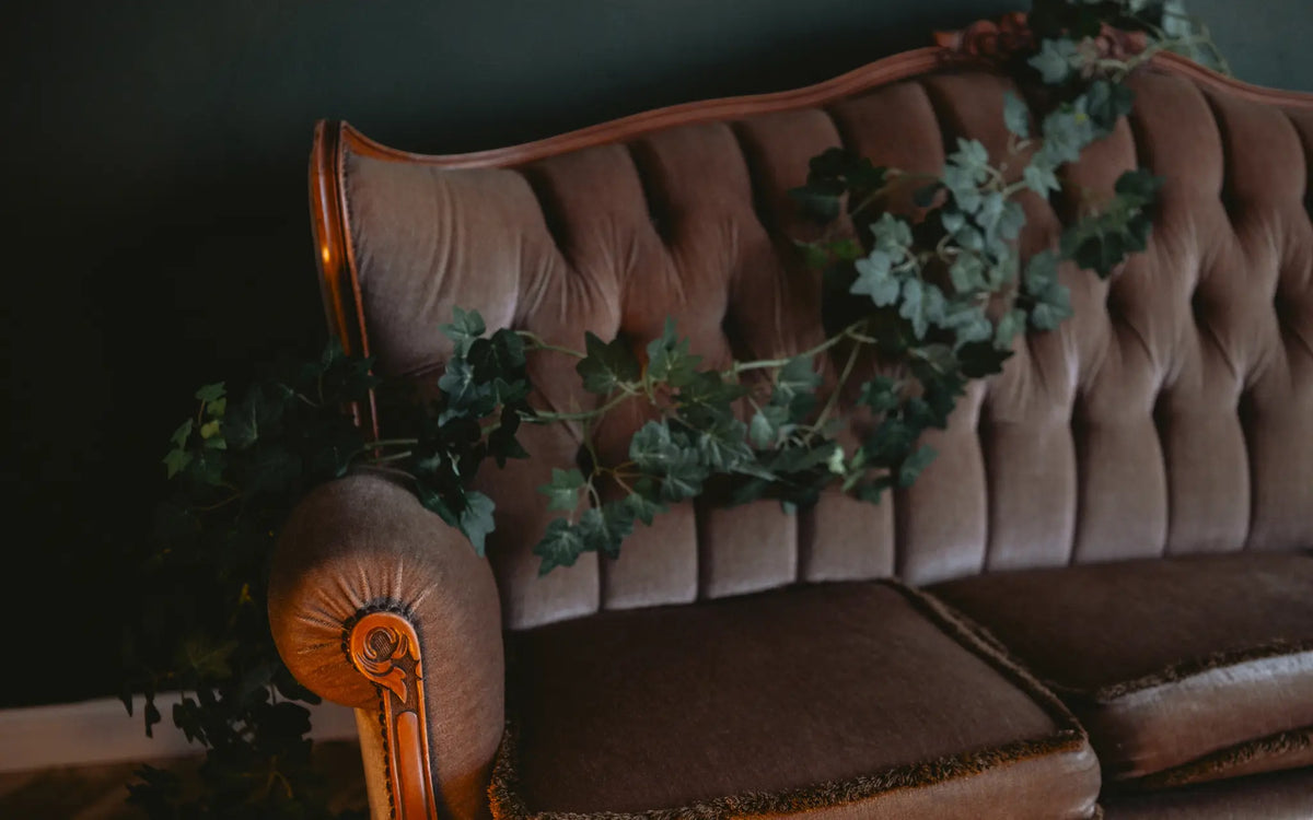 Vintage-Sofa mit Knopfpolsterung und Efeublättern in schwachem Zimmerlicht.